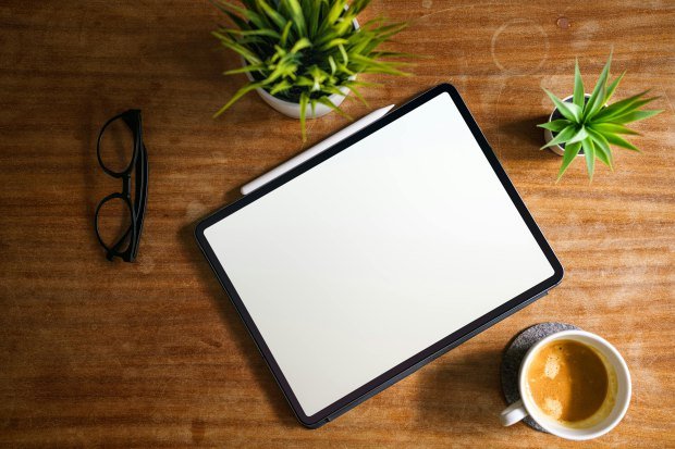 A flat lay of a tablet, coffee, and plants on a wooden desk, ideal for creative workspaces.